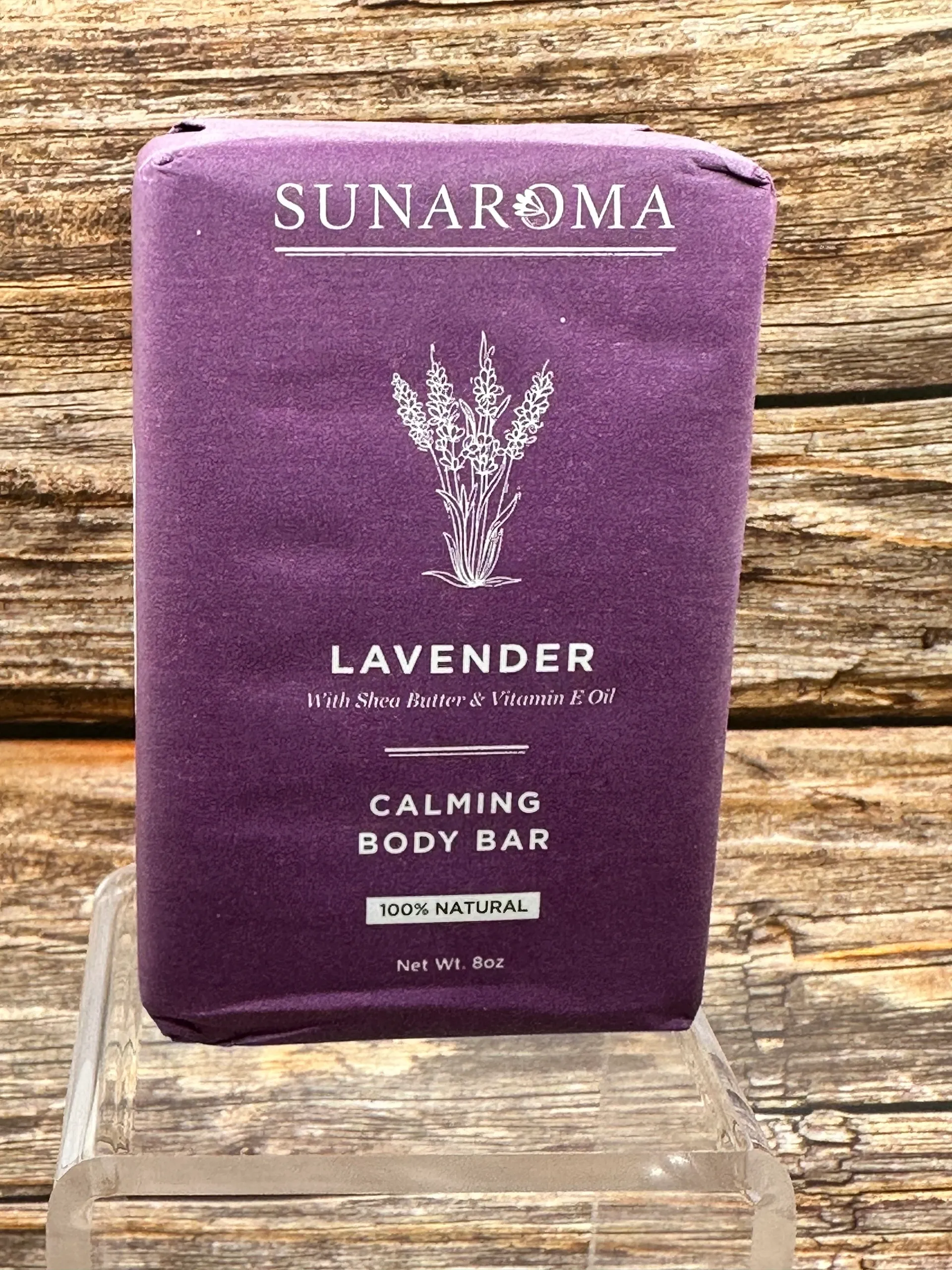 Lavender calming body bar placed on a glass stand against a wooden wall