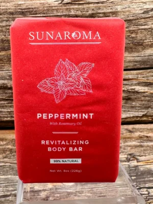 Red box of Sunaroma Peppermint Revitalizing Body Bar on a glass stand, with a wooden wall in the background
