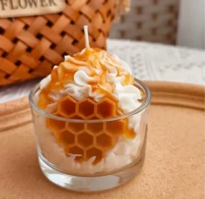 Glass filled with a honeycomb-shaped candle on top of a table, with a basket of honey beside it